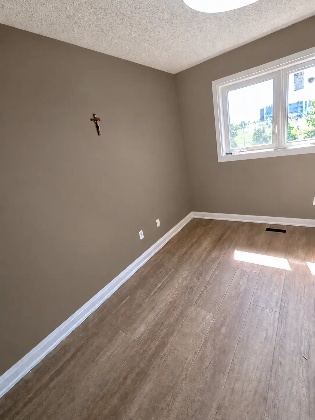 Refined vacant room with warm beige walls, clean white trim and wood-look flooring